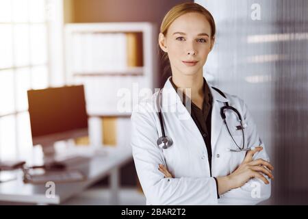 Une femme souriante et gaie se tenant debout avec les bras croisés dans la clinique. Portrait d'une femme médecin sympathique. Concept de médecine Banque D'Images