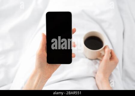 Femme utilisant un téléphone portable avec écran vide dans le lit Banque D'Images