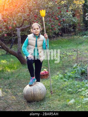 Bonne fille dans le jardin. La fille tient une pomme de la récolteuse. La fille se tient près d'une grande citrouille Banque D'Images