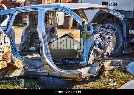 vieux cadre gris voiture démontée voiture avec des pièces rouillées dans la rue près de la clôture. Banque D'Images
