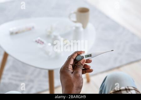 Traitement des maladies contagieuses. Homme d'Afrique senior avec thermomètre montrant la température de la fièvre à l'intérieur, gros plan Banque D'Images