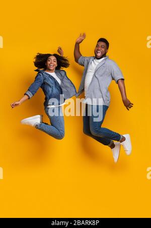 Liberté. Couple noir joyeux sautant dans l'air sur fond jaune Banque D'Images