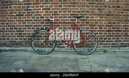 Vélo à engrenage fixe Singlespeed rouge de style rétro isolé sur un mur de briques Banque D'Images