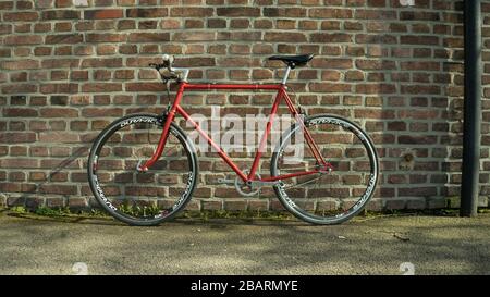 Vélo à engrenage fixe Singlespeed rouge de style rétro isolé sur un mur de briques Banque D'Images