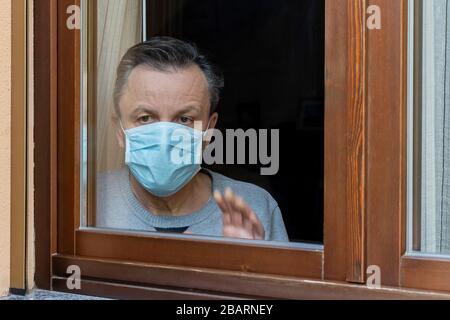 Homme italien avec masque de protection, forcé de rester à la maison en raison du coronavirus covid-19, disconsolate regarde la fenêtre de la maison Banque D'Images