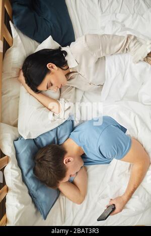 Au-dessus de la vue portrait de jeune couple moderne dormant avec l'homme en utilisant le smartphone à côté de la femme, copier l'espace Banque D'Images
