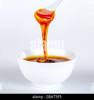 le miel s'écoule de la cuillère en céramique à la cuvette en céramique Banque D'Images