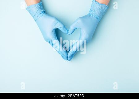 Les mains du médecin dans des gants médicaux en forme de coeur sur fond bleu avec espace de copie. Banque D'Images