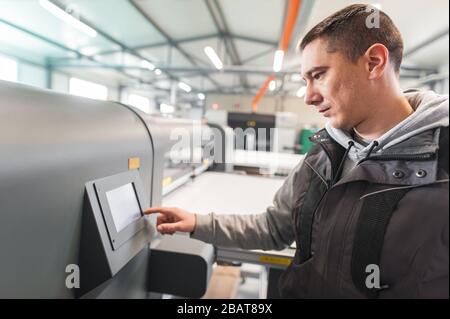 L'opérateur du technicien du fabricant d'impression travaille dans une grande salle de presse d'impression numérique et un bureau de magasin d'impression avec de nombreux types de machine différents Banque D'Images