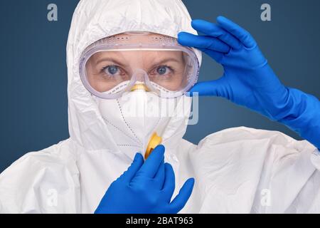 Concept de coronavirus. Médecin en costume de noisette gants médicaux et respirateur debout isolé sur le bleu de contrôle unifrom concerné gros plan Banque D'Images