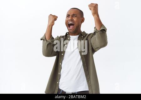 Portrait d'un homme afro-américain heureux et triomphant célébrant la victoire, pari gagnant de fan de football dans le jeu sportif, levant les mains gaies, enracinement Banque D'Images