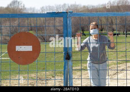 Les femmes caucasiennes se trouvent dans un masque de protection derrière une porte fermée avec un panneau rouge d'arrêt. En quarantaine pour le covid-19 du coronavirus. Concept de séjour à la maison Banque D'Images