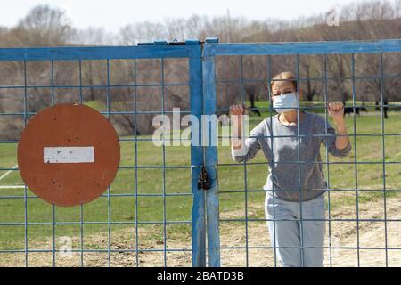 Les femmes caucasiennes se trouvent dans un masque de protection derrière une porte fermée avec un panneau rouge d'arrêt. En quarantaine pour le covid-19 du coronavirus. Concept de séjour à la maison Banque D'Images