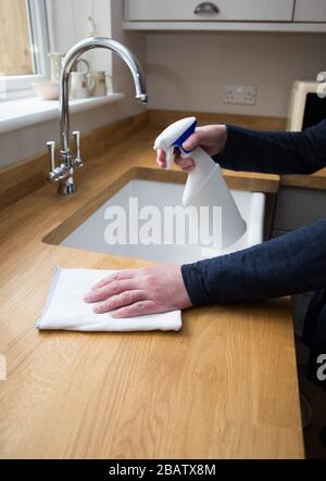 Un gros plan d'une paire de mains humaines nettoyant l'intérieur d'une cuisine avec un spray antibactérien pour désinfecter les surfaces de travail pendant le Coronavirus Banque D'Images