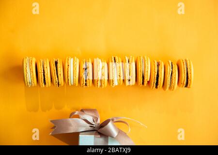 Vue de dessus de délicieux macarons jaunes d'orange et de boîte cadeau. Concepts idées contexte sur papier jaune, planéité et espace de copie Banque D'Images