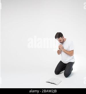 Jeune homme isolé en arrière-plan. Guy se tiennent sur les genoux et prient en face de la Bible. Étudier la parole de Dieu. Croire ou foi en Jésus-Christ. Banque D'Images