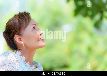 Gros plan sur le côté d'une femme asiatique en bonne santé d'âge moyen habille dans des vêtements de style thaïlandais, Portrait vieille dame se reposant à l'extérieur regardant sourire heureux dans le