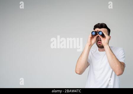 Jeune homme isolé en arrière-plan. Guy regarder des jumelles loin vers l'avant. Autonome en studio. Un gars décontracté à l'image. Enquête. Banque D'Images