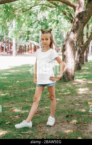 Fille enfant portant un t-shirt blanc vierge avec de l'espace pour votre logo ou design posant dans le parc Banque D'Images