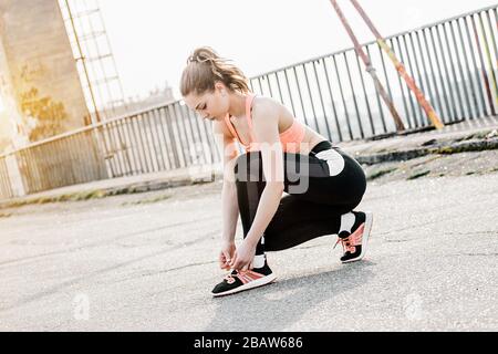 Jolie jeune femme de sport assise sur la route et lacets pour chaussures de ficelage sur les baskets avant le jogging du matin. Belle fille de forme physique sportive dans l'élégance de l'espionnage Banque D'Images