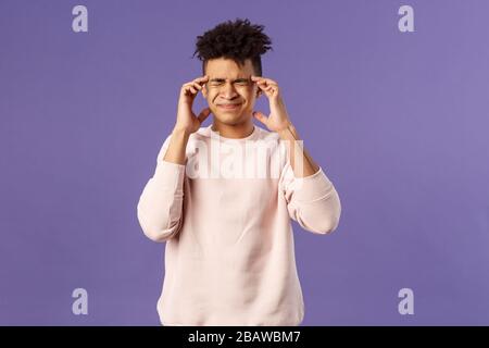 Portrait de jeune étudiant masculin intense et pressé surtravaillé, se sentir fatigué et étourdi, grimaçant de sensation douloureuse dans la tête, ayant mal de tête ou migraine Banque D'Images