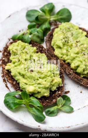 Pain de seigle avec purée d'avocat et de graines de chanvre. Toast végétalien sain sur plaque blanche Banque D'Images