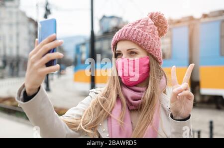 Femme faisant signe de victoire rendant selfie avec le téléphone porter masque Banque D'Images