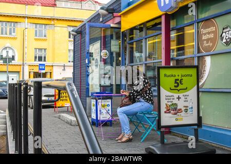 Une femme est assise et écrit dans une petite table extérieure patio à l'extérieur d'un magasin de proximité à Porvoo, en Finlande. Banque D'Images