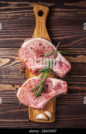 Steak de porc aux épices et au romarin. Viande crue fraîche et juteuse avec des grains de poivre sur une planche à découper en bois sur le plan de travail de la cuisine photo verticale Banque D'Images