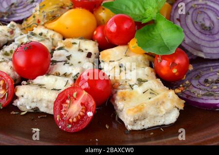 Petit-déjeuner grec feta grillée, dans brown plaque en céramique avec quelques légumes et épices, oignon rouge, jaune et rouge, de tomates cerises et de basilic frais Banque D'Images