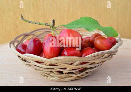 Cerises de cornéennes fraîches dans un petit panier en osier sur la table, sur fond de bois Banque D'Images