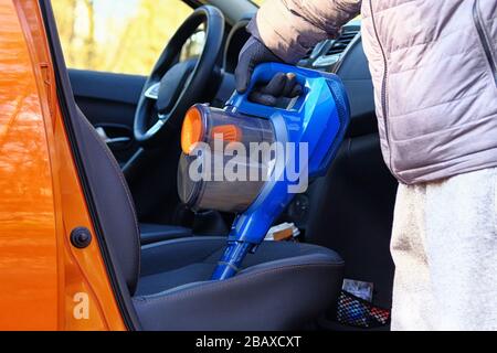 Aspirateur entre les mains du conducteur. Nettoyage de l'intérieur de l'automobile avec aspirateur bleu. Les sièges en textile de voiture sont régulièrement nettoyés. Banque D'Images