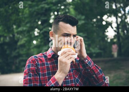 Beau jeune homme mangeant sandwich autodoor. Il tient un téléphone Banque D'Images
