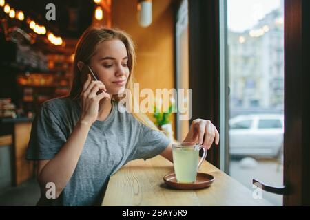 La blonde utilise le téléphone. Fille et smartphone. Une femme est assise dans un café avec un cellulaire Banque D'Images