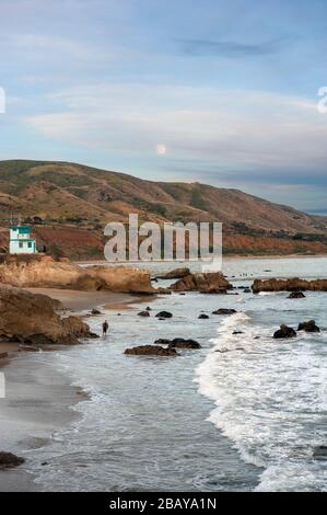 Homme marchant sur une plage de Malibu avec la pleine lune qui monte sur les collines côtières le long de la côte de la Californie du Sud, États-Unis Banque D'Images
