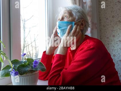 Le concept de santé, de sécurité et de pandémie du Covid-19 - une vieille femme solitaire séniée près de la fenêtre Banque D'Images
