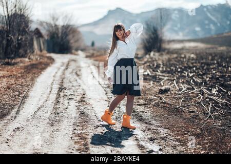 Une belle jeune femme dans une jupe grise et des bottes en caoutchouc marche à travers un pré dans le pays. Elle danse, rire a plaisir et rayonne la liberté Banque D'Images