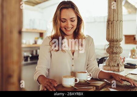 Femme souriante debout derrière le comptoir café d'un café. Barista féminin souriant servant deux tasses de café. Banque D'Images