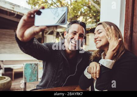 Homme prenant selfie avec une femme montrant son anneau d'engagement tout en étant assis au café. Couple affectueux qui se fait selfie avec l'anneau d'engagement. Banque D'Images