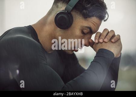 Jeune homme dans des vêtements de sport avec casque prenant une pause. Jeune homme se sentant fatigué après un entraînement intense. Banque D'Images