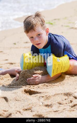 Garçon caucasien de 6 ans portant des groupes de bras de flottabilité ayant du plaisir à jouer dans la plage de sable chaud sur les vacances Varna Bulgarie Banque D'Images