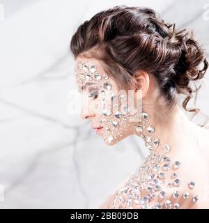 Maquillage inhabituel et art du visage avec des strass étincelants sur la peau. Une fille avec des cristaux précieux sur son visage, une image de mode dans des couleurs légères et douces. Banque D'Images