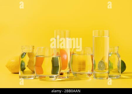 Citron d'agrumes et chaux déformés à travers de l'eau liquide dans le verre sur jaune. Gros plan. Concept tropical créatif. Banque D'Images