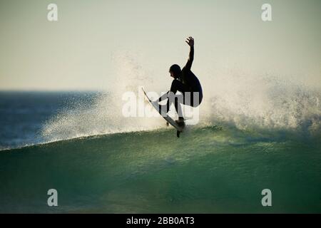 Un surfeur solitaire qui attrape des vagues dans l'océan Atlantique à la plage de Llandudno sur le cap occidental silhoueté par le soleil couchant. Banque D'Images