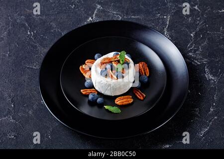 Fromage blanc doux mûri aux bleuets, pacanes à la menthe sur une plaque noire sur fond en béton foncé, gros plan Banque D'Images