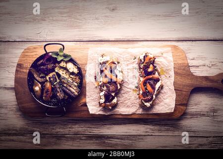 Tranches de pain rustiques sur l'ancienne planche en bois avec légumes grillés et herbes, style vintage et rétro, couleurs vives, plat végétarien, vue sur le dessus Banque D'Images