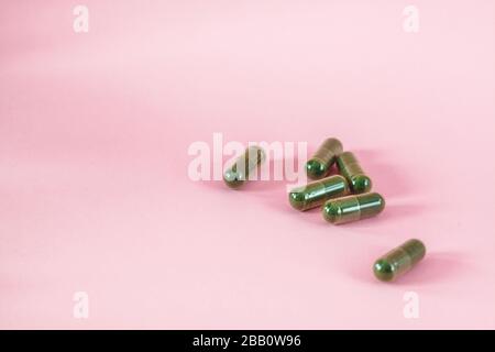 Spiruline ou chlorella en capsules sur fond rose. Banque D'Images