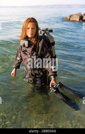 Une femme instructeur de plongée sous-marine debout dans l'eau portant un costume sec, un réservoir double et des palmes de maintien Banque D'Images