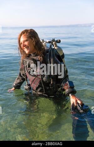 Une femme instructeur de plongée sous-marine debout dans l'eau portant un costume sec, un réservoir double et des palmes de maintien Banque D'Images