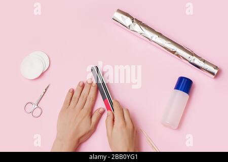 Les mains des femmes éliminent le vernis à ongles sur fond rose. Concept de manucure à domicile. Banque D'Images